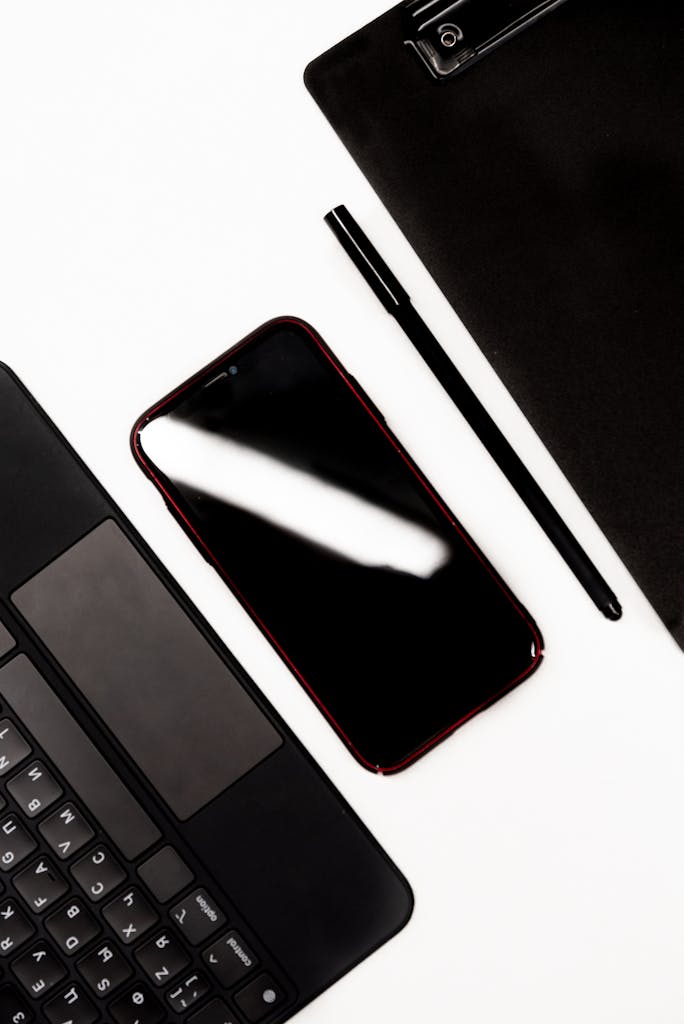 Flat lay of a smartphone, laptop, pen, and clipboard on a desk.